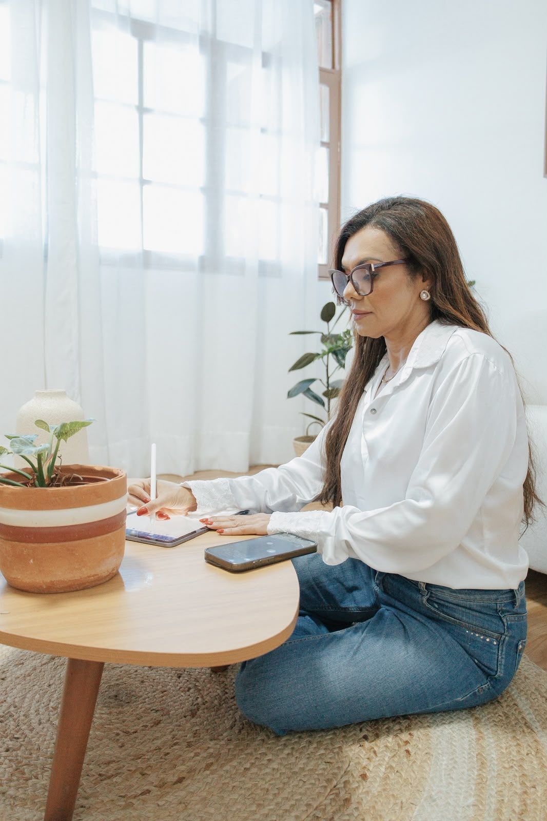 Sandra fazendo anotações em uma mesa de centro, ao lado de um vaso de flores